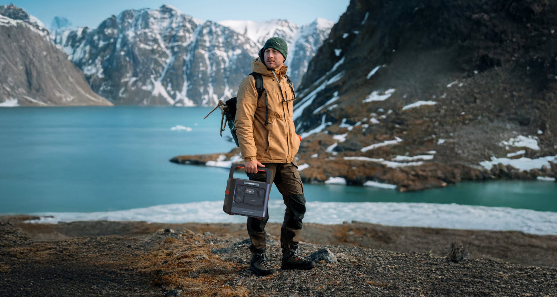 Hiker carrying the Jackery Explorer 1500 Ultra by its handle beside a glacial mountain lake