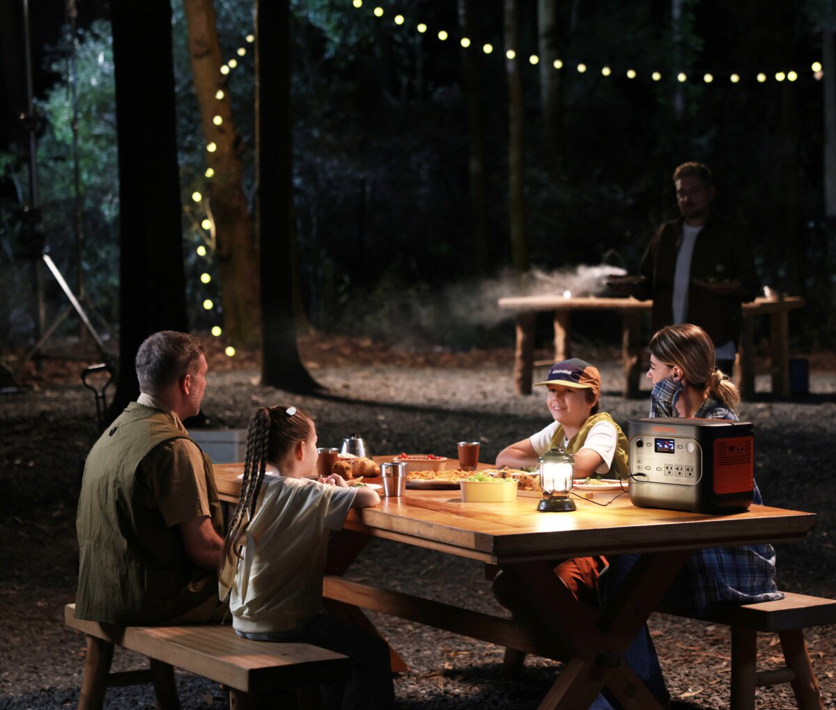 Family gathered at a nighttime campsite picnic table with the Explorer 1500 v2 powering a lantern