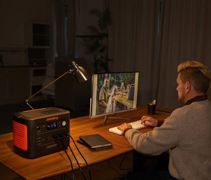 Man working at a home office desk at night with the Explorer 1500 v2 powering a lamp and monitor