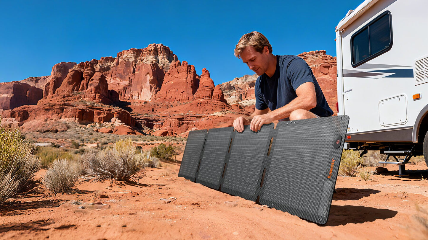 Man setting up folded 100W Air solar panel on red desert sand beside an RV