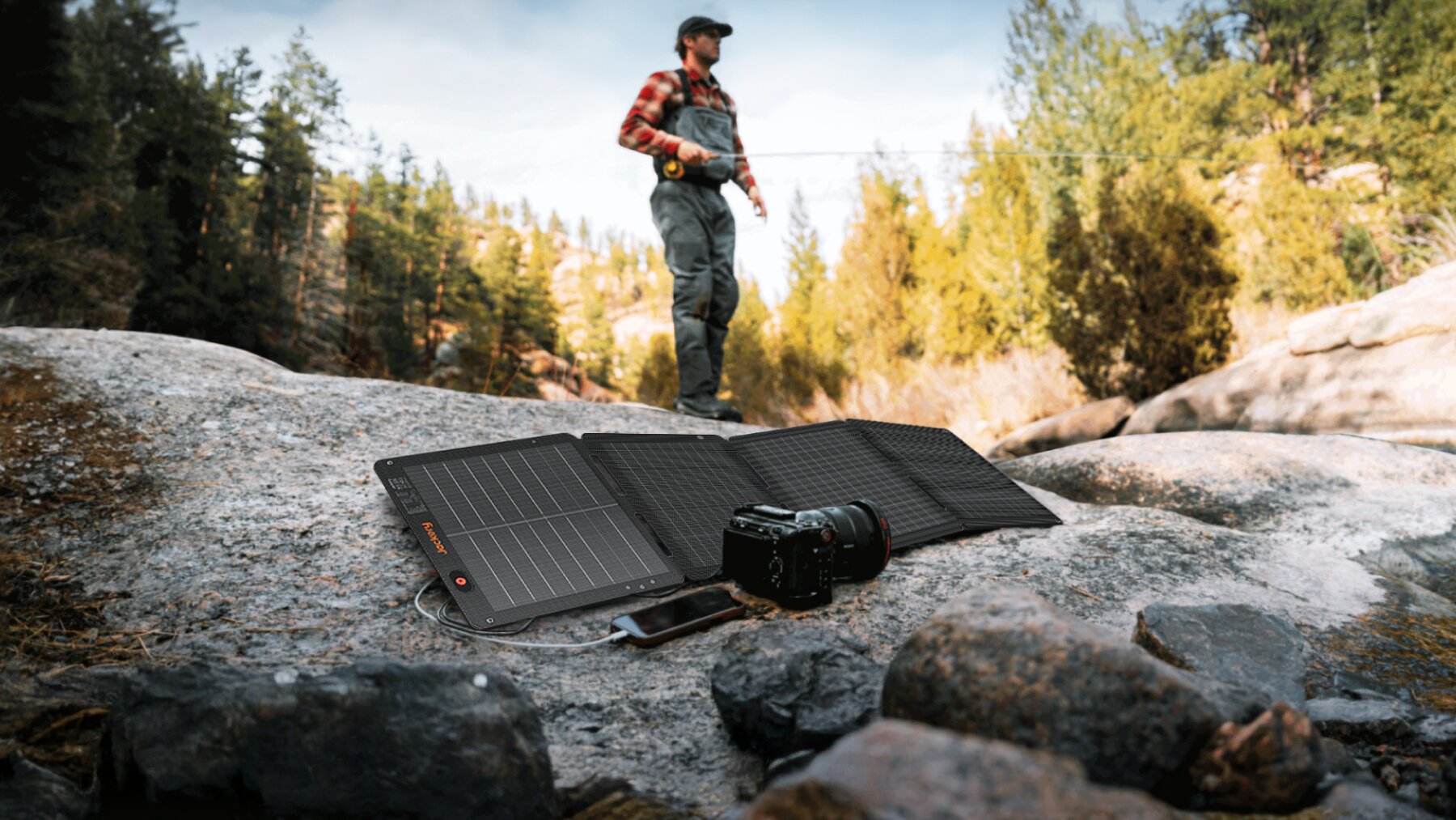 100W Air solar panel unfolded on rocks charging a phone and camera during outdoor fishing trip