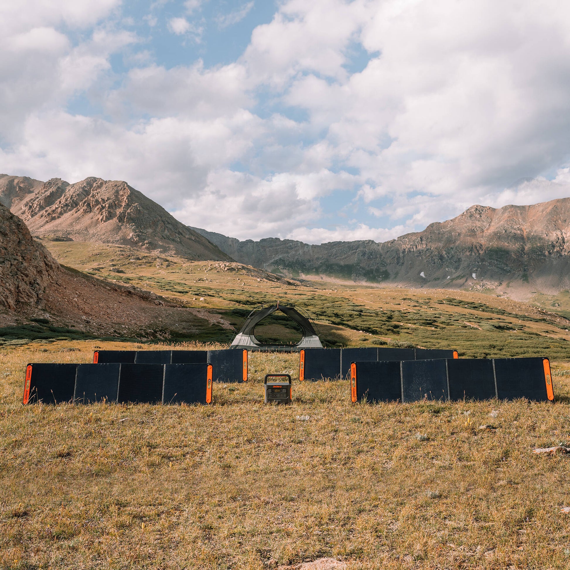 Four SolarSaga 200W panels arranged in a rectangle around a power station in a mountain meadow campsite