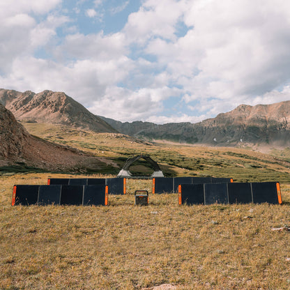 Four SolarSaga 200W panels arranged in a rectangle around a power station in a mountain meadow campsite