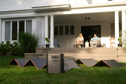 HomePower 3600 Plus with four folding solar panels on a lawn while a couple relaxes on a porch at golden hour