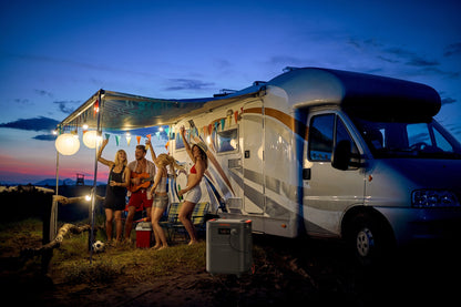Friends dancing and playing guitar under string lights next to an RV powered by HomePower 3600 Plus at dusk