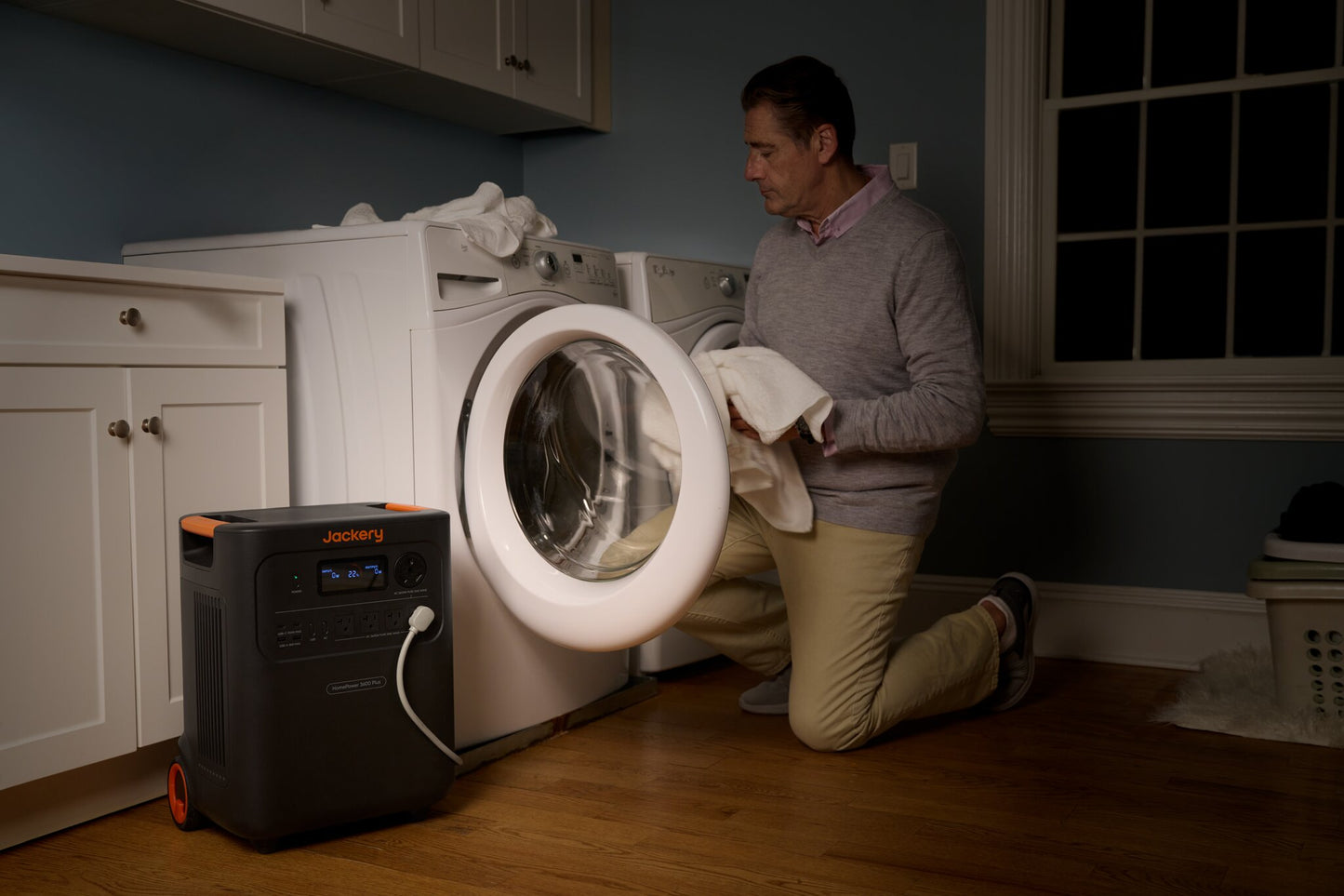 Man kneeling at an open front-load washing machine with HomePower 3600 Plus powering the laundry room