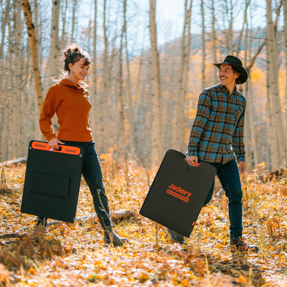 Two people carrying folded SolarSaga 200W solar panels through an autumn forest